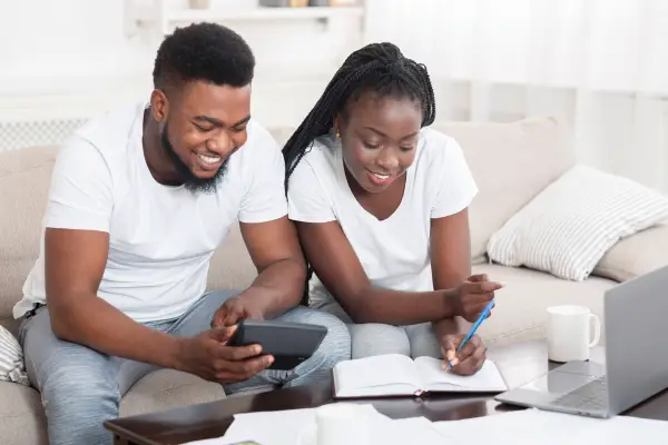 black couple sitting on sofa happy while managing finances